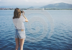 Hipster photograph on vintage camera or technology, mock up. Girl using vintage camerae on blue sea and yacht background close photo