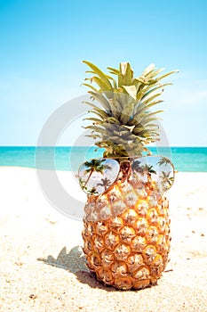 Hipster pineapple with sunglasses on a sandy beach.