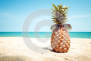 Hipster pineapple with sunglasses on a sandy at tropical beach.