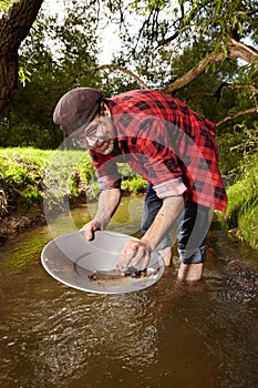 Hipster prospector panning sand in creek for gold