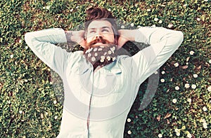 Hipster on relaxed face lays on grass, top view. Appeasement concept. Guy looks nicely with daisy or chamomile flowers