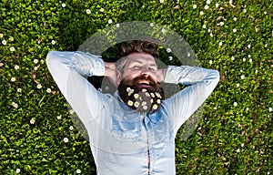 Hipster on smiling face lays on grass, top view. Man with beard and mustache enjoys spring, green meadow background