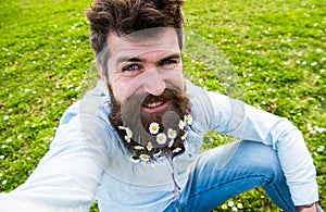 Hipster on smiling face sits on grass, defocused. Natural beauty concept. Man with beard enjoys spring, green meadow