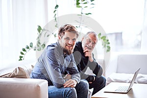 Hipster son and his senior father with laptop at home.