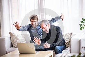 Hipster son and his senior father with laptop at home.