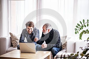 Hipster son and his senior father with laptop at home.