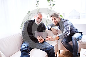 Hipster son and his senior father with tablet at home.