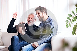 Hipster son and his senior father with tablet at home.