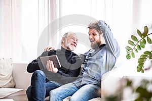 Hipster son and his senior father with tablet at home.