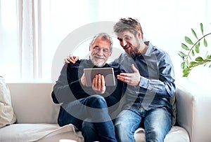 Hipster son and his senior father with tablet at home.