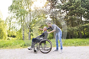 Hipster son walking with disabled father in wheelchair at park.