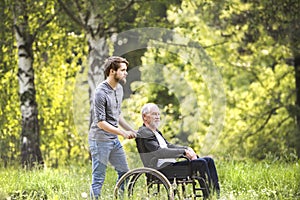 Hipster son walking with disabled father in wheelchair at park.