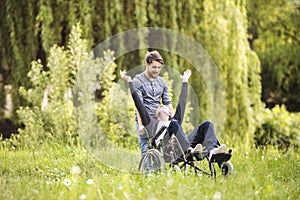 Hipster son walking with disabled father in wheelchair at park.