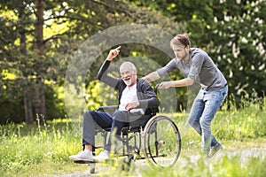 Hipster son walking with disabled father in wheelchair at park.