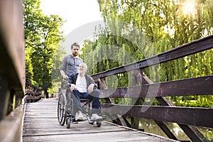 Hipster son walking with disabled father in wheelchair at park.