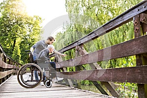 Hipster son walking with disabled father in wheelchair at park.