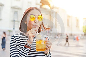 Hipster student drinks a cool lemonade through a straw in a summer outdoor cafe