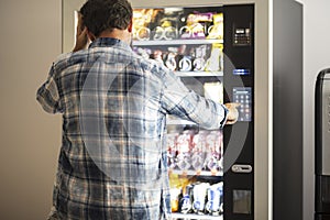 Hipster style man viewed from back buying snacks or drink from vending automatic machine typing product code. People and travel