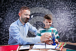 Hipster teacher with his student with microscope, big blackboard