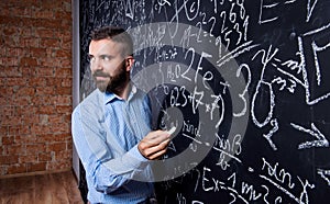 Hipster teacher writing on big blackboard with mathematical symbols