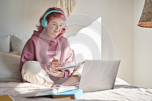 Hipster teen girl student with pink hair watch online webinar learning in bed.