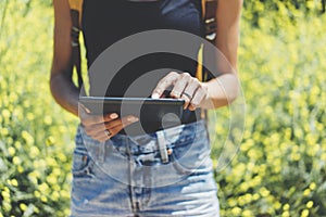 Hipster texting message on tablet or technology, mock up of blank screen. Girl using computer on yellow flowers background close