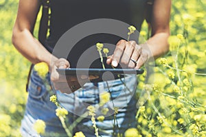 Hipster texting message on tablet or technology, mock up of blank screen. Girl using computer on yellow flowers background close