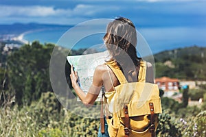 Hipster tourist hold and look map on trip, lifestyle concept adventure, traveler with backpack on background mountain and blue sea