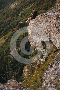 Hipster traveler sitting on top of rock mountain and enjoying amazing view on river. Young guy exploring and traveling.