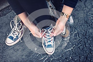 Hipster wearing sneakers, teenager tieing laces at sport shoes. Urban lifestyle with footwear and modern clothing.