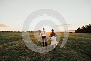 Hipster wedding couple running on a field in sunset light in fog