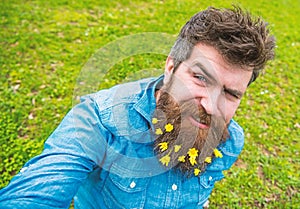 Hipster on winking face sits on grass, defocused. Man with beard enjoys spring, green meadow background. Guy with lesser