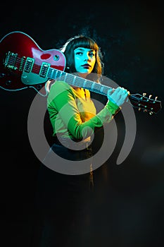 Hipster woman with curly hair with red guitar in neon lights. Rock musician with electrical guitar. 90s style concept.