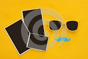Hipster yellow sunglasses and funny moustache next to blank photographs