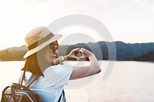 Hipster young asian woman showing hands heart shape at nature sunset,Travel insurance concept