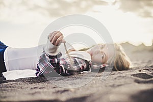 Hipster young cute blonde caucasian girl play with the sand at the beach - lay down people in vacation leisure activity - golde