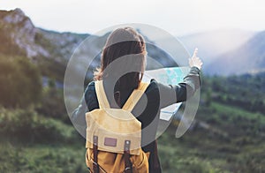 Hipster young girl with backpack enjoying sunset on peak of foggy mountain, looking a map and poining hand. Tourist traveler