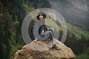 Hipster young girl with backpack enjoying sunset on peak mountain. Tourist traveler on background valley landscape view