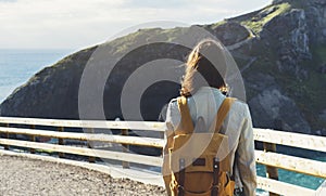Hipster young girl with backpack enjoying sunset on seascape on peak mountain. Tourist traveler on background valley