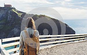 Hipster young girl with backpack enjoying sunset on seascape on peak mountain. Tourist traveler on background valley landscape