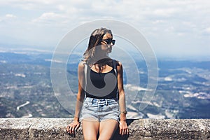 Hipster young girl with backpack and sunglasses looking on observation deck and planning travel plan. View tourist traveler