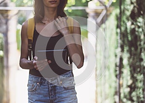 Hipster young girl with backpack using tablet computer, hands holding gadget and texting message on device. View tourist traveler