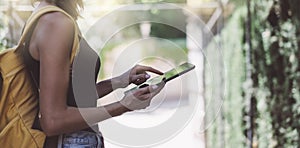 Hipster young girl with backpack using tablet computer, hands holding gadget and texting message on device. View tourist traveler