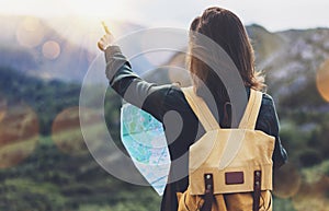 Hipster young girl with bright backpack enjoying sunset on peak of foggy mountain, looking a map and poining hand. Tourist travel