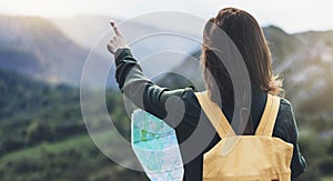 Hipster young girl with bright backpack enjoying sunset on peak of foggy mountain, looking a map and poining hand. Tourist travele