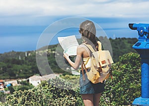 Hipster young girl with bright backpack looking at a map and poining hand the travel plan. View from the back of the tourist