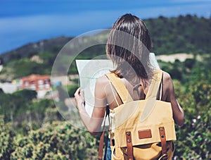 Hipster young girl with bright backpack looking at a map and poining hand the travel plan. View from the back of the tourist