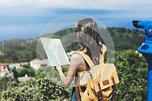 Hipster young girl with bright backpack looking at a map and poining hand the travel plan. View from the back of the tourist trave