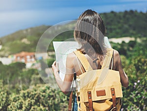 Hipster young girl with bright backpack looking at a map and poining hand the travel plan. View from the back of the tourist trave