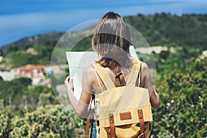 Hipster young girl with bright backpack looking at a map and poining hand the travel plan. View from the back of the tourist